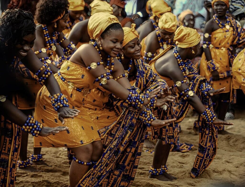N'zima dancers in orange and blue, wearing bead bracelets, at the Abissa festival in Grand-Bassam